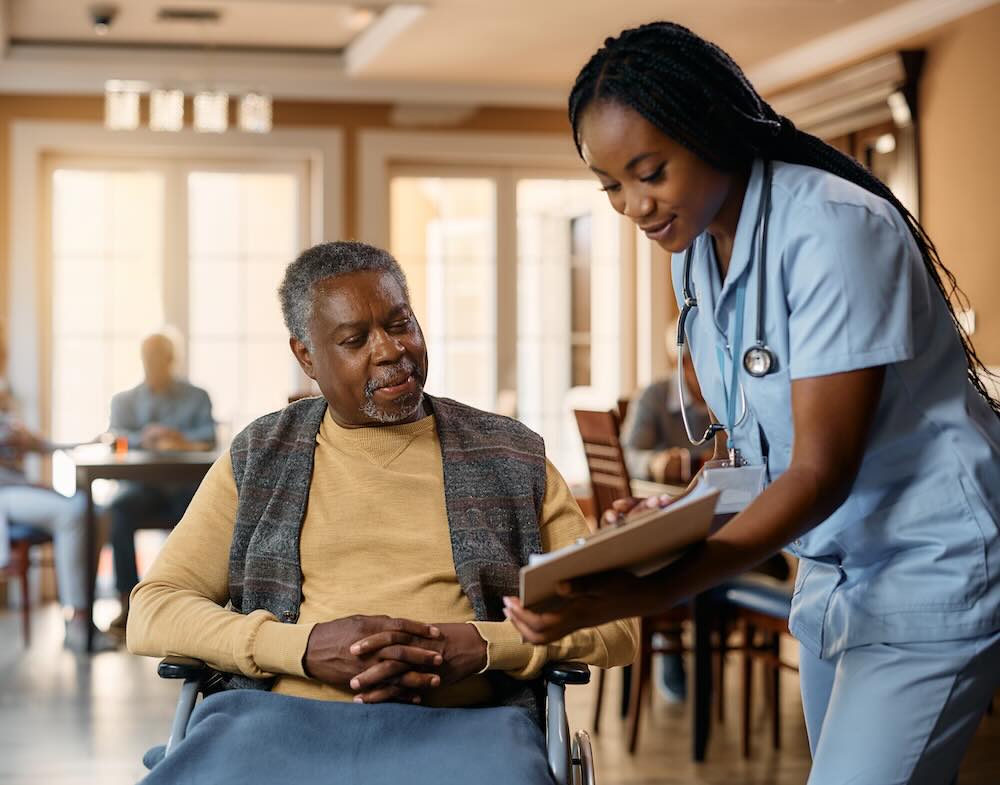 Senior black man in wheelchair and young nurse analyzing medical paperwork at nursing home.