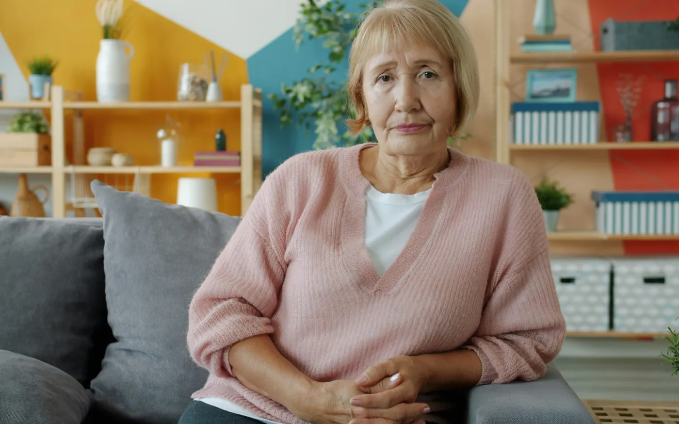 Elderly woman sitting on a couch in a living room. by Vitaly Gariev courtesy of Unsplash.