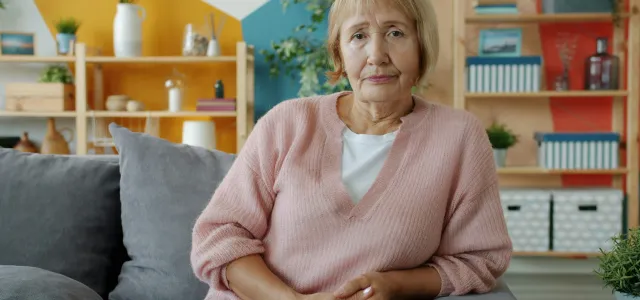 Elderly woman sitting on a couch in a living room. by Vitaly Gariev courtesy of Unsplash.