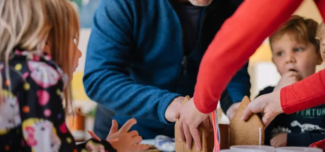 two person making gingerbread house and three children watching them by Phillip Goldsberry courtesy of Unsplash.